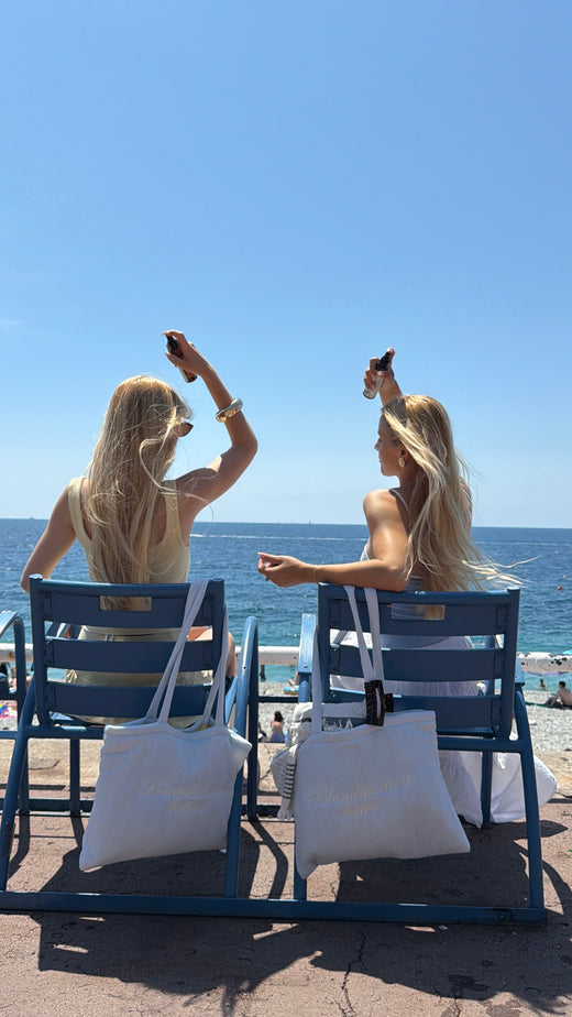 Deux blondies face a la mer avec le spray et les tote bags OMAD'S